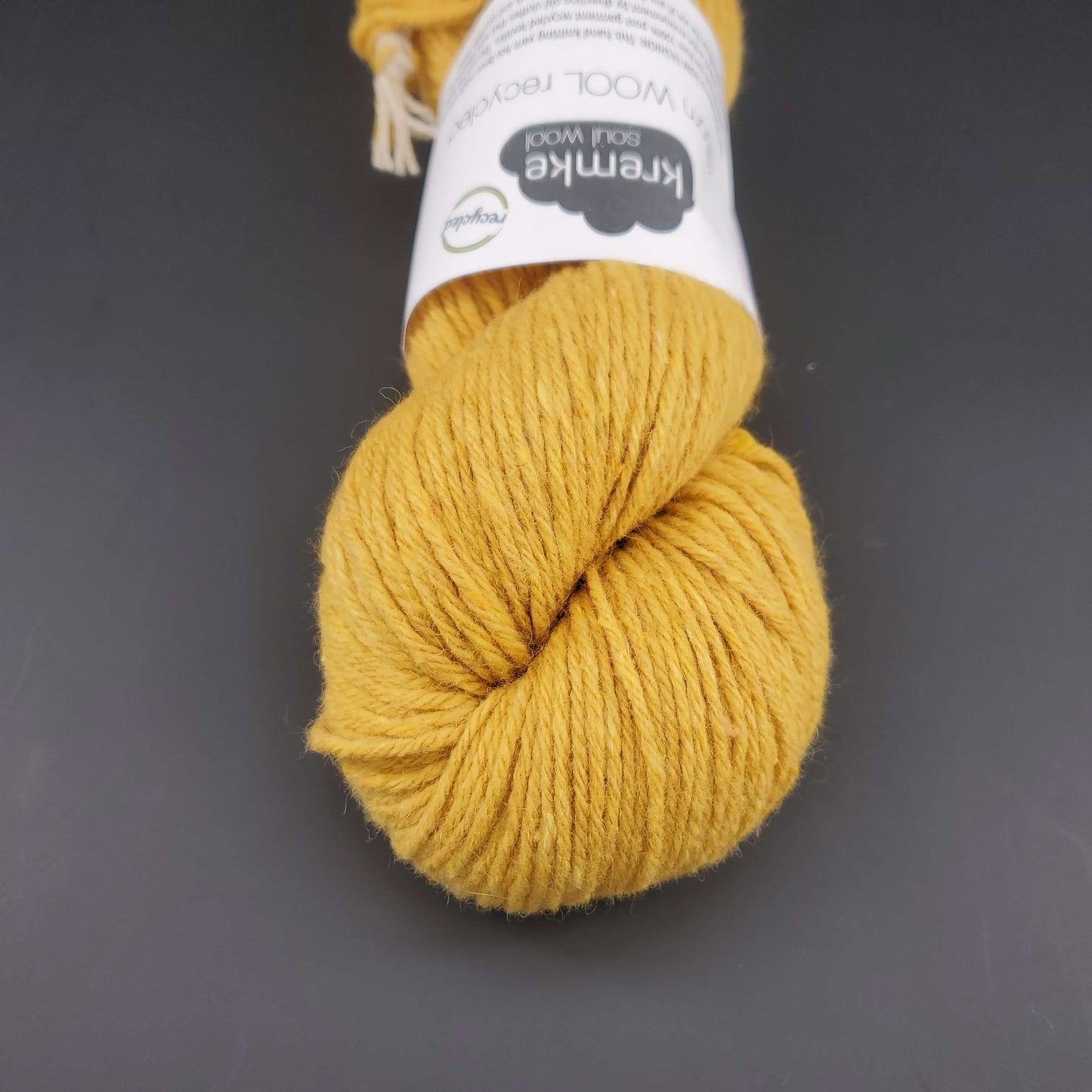 Echeveau de laine Kremke Reborn Wool de couleur 06 golden yellow, sur fond noir, pour tricot et crochet.