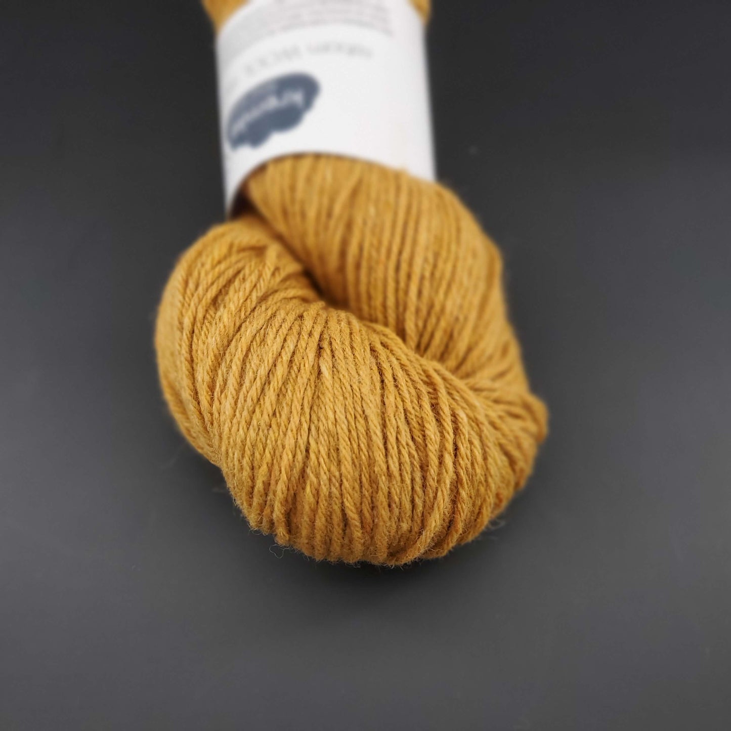 Echeveau de laine Kremke Reborn Wool de couleur 07 mustard yellow, sur fond noir, pour tricot et crochet.