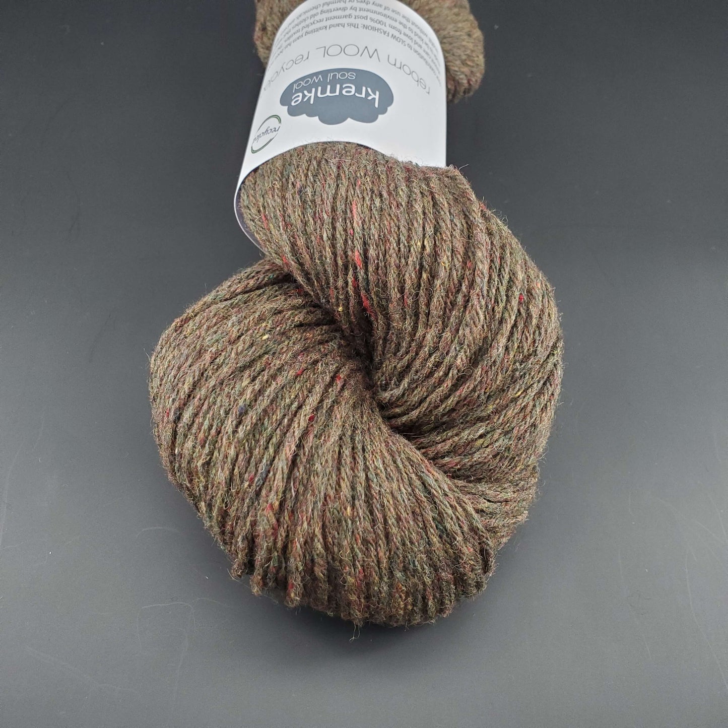 Echeveau de laine Kremke Reborn Wool de couleur 13 olive melange, sur fond noir, pour tricot et crochet.