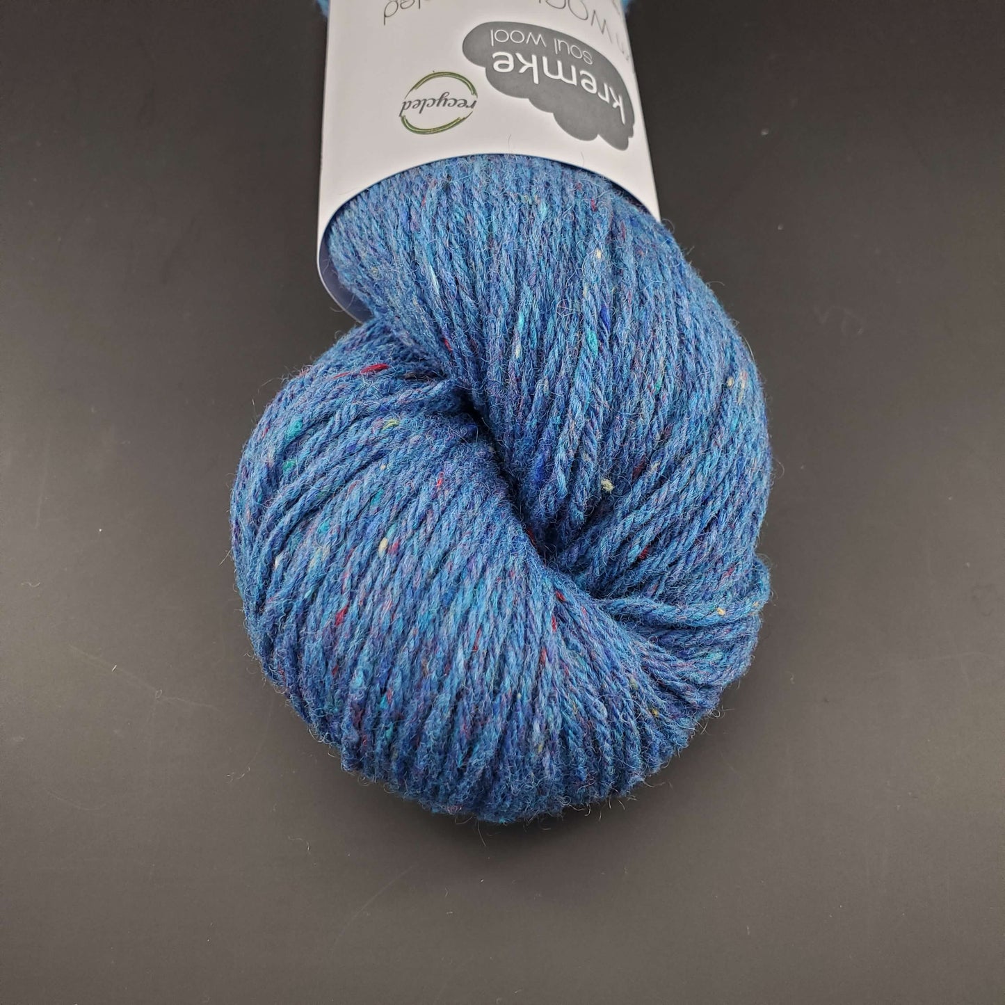 Echeveau de laine Kremke Reborn Wool de couleur 19 ocean melange, sur fond noir, pour tricot et crochet.