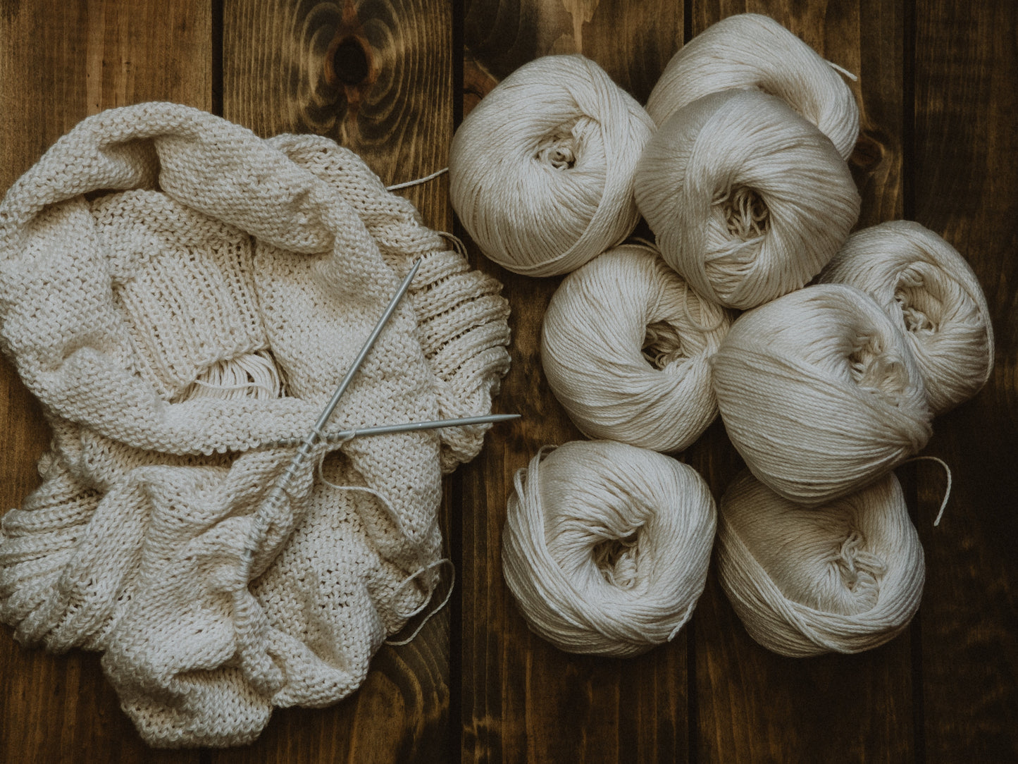 tas de pelotes de laine écrues à côté d'un ouvrage en cours de tricot de la même couleur