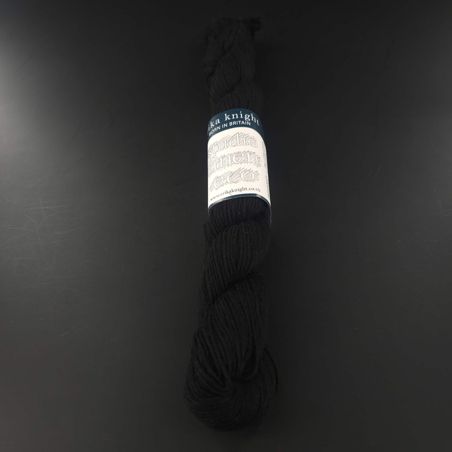 Echeveau de lin Studio Linen Eco d'Erika Knight de couleur 411 Kumo (noir) sur fond noir pour tricot et crochet.
