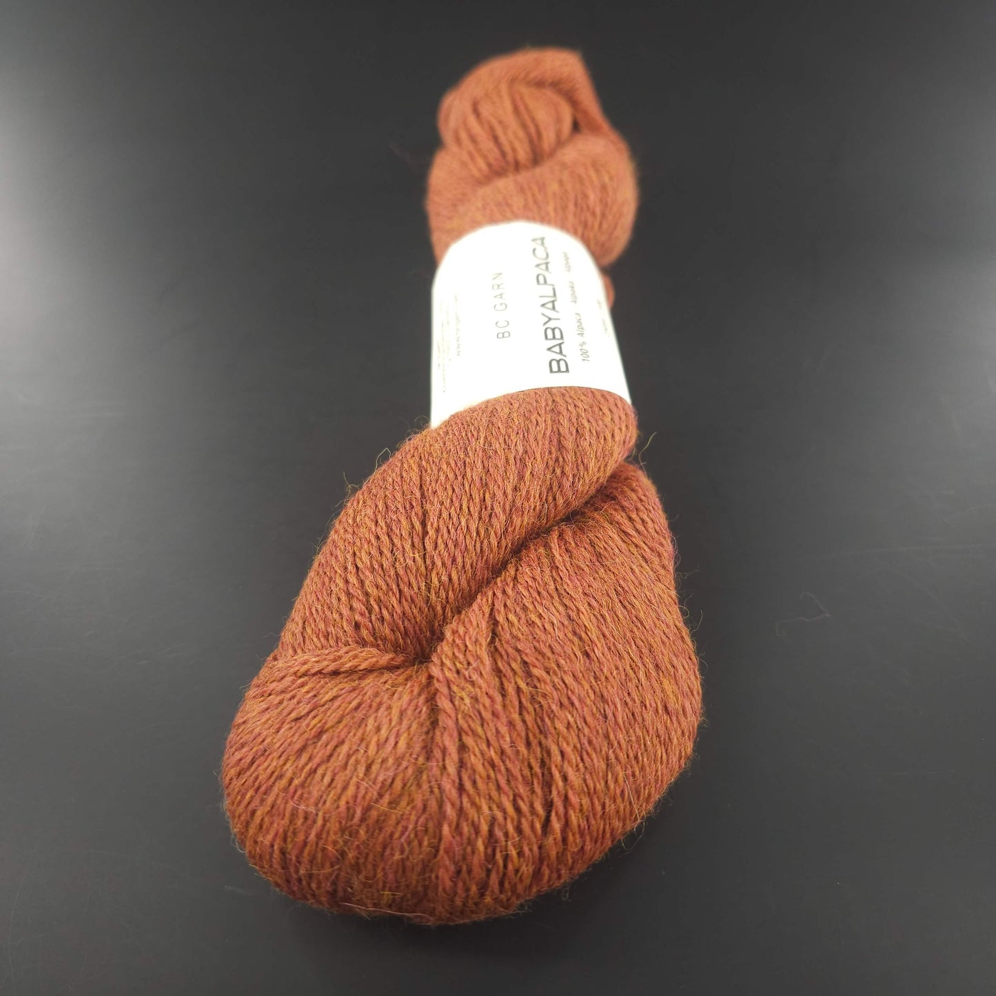 Echeveau de laine Baby Alpaca de BC Garn de couleur 125 rust melange sur fond noir.