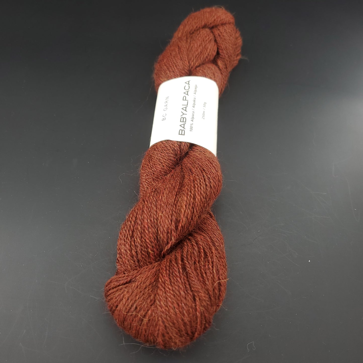 Echeveau de laine Baby Alpaca de BC Garn de couleur 125 redbrown melange sur fond noir.
