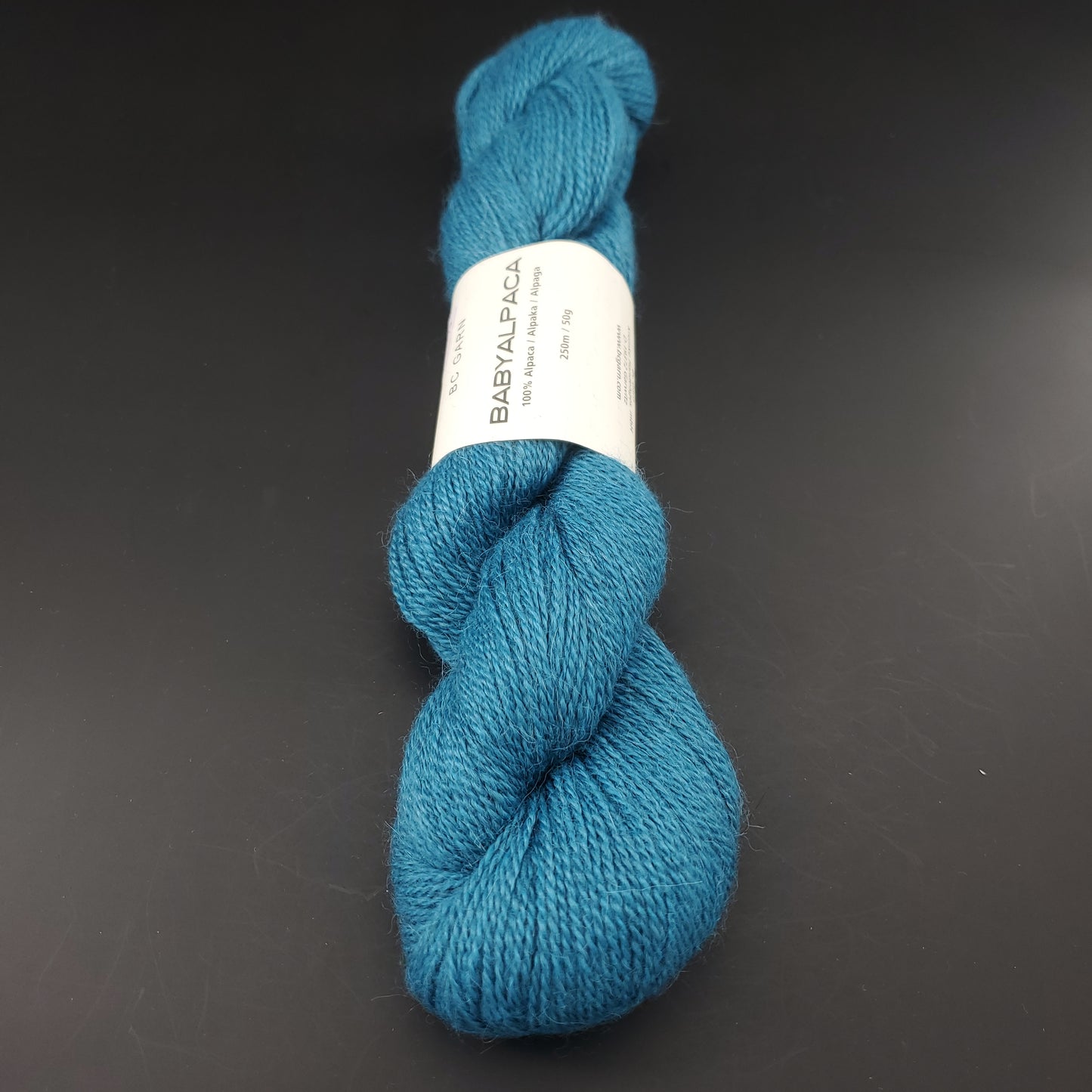 Echeveau de laine Baby Alpaca de BC Garn de couleur 53 petrol sur fond noir.