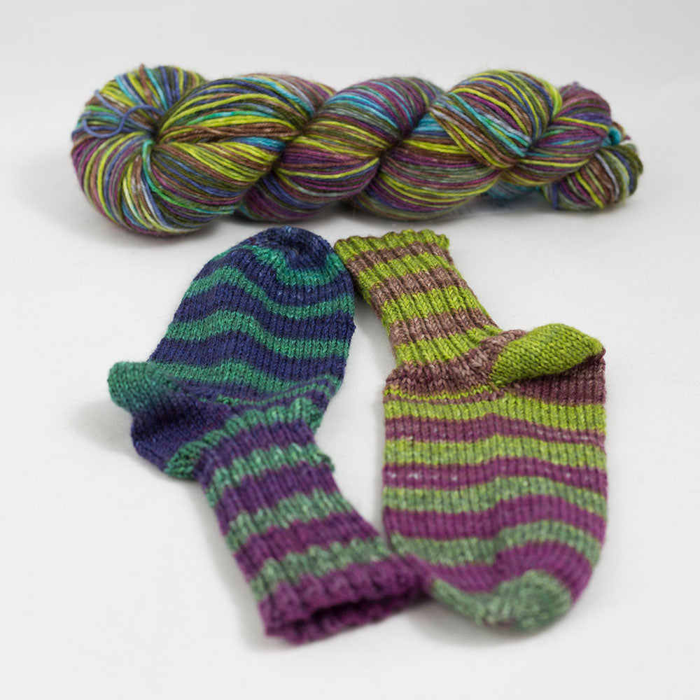 écheveau de laine à chaussettes Lazy Lion, multicolore, marque Kremke et paire de chaussettes tricotées (vert, violet, bleu)